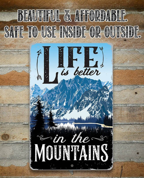 A rectangular metal sign with a mountain landscape print and the words “LIFE is better in the MOUNTAINS,” shown against a rustic wood plank background. Above the sign, additional text reads “BEAUTIFUL & AFFORDABLE.
