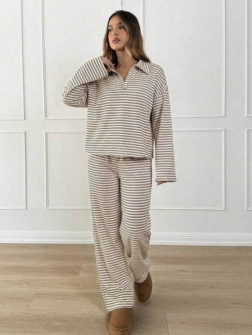 Woman wearing a striped pajama set in a room with wooden flooring and white paneled walls.