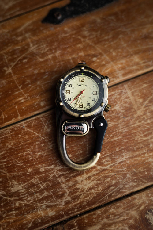 Vintage-style pocket watch with carabiner on a wooden surface