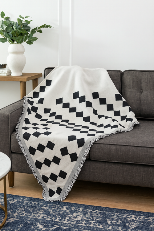 A black and white diamond-patterned throw blanket with fringe edges draped over a gray sofa in a living room setting.