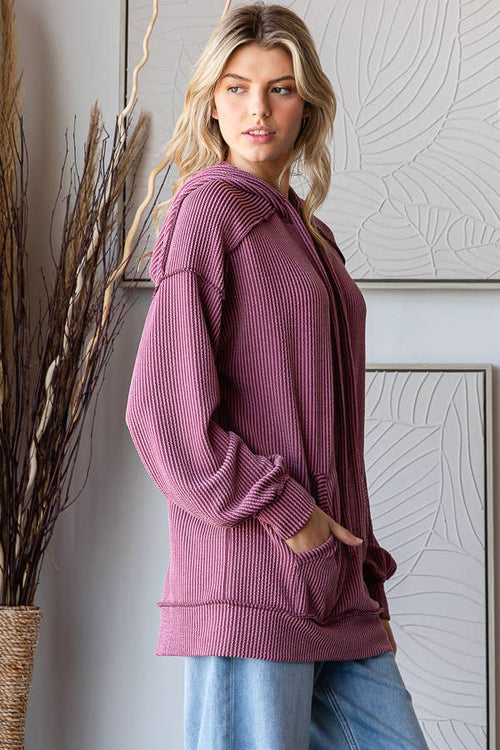 Woman wearing a pink ribbed sweater standing in a room with decorative elements.