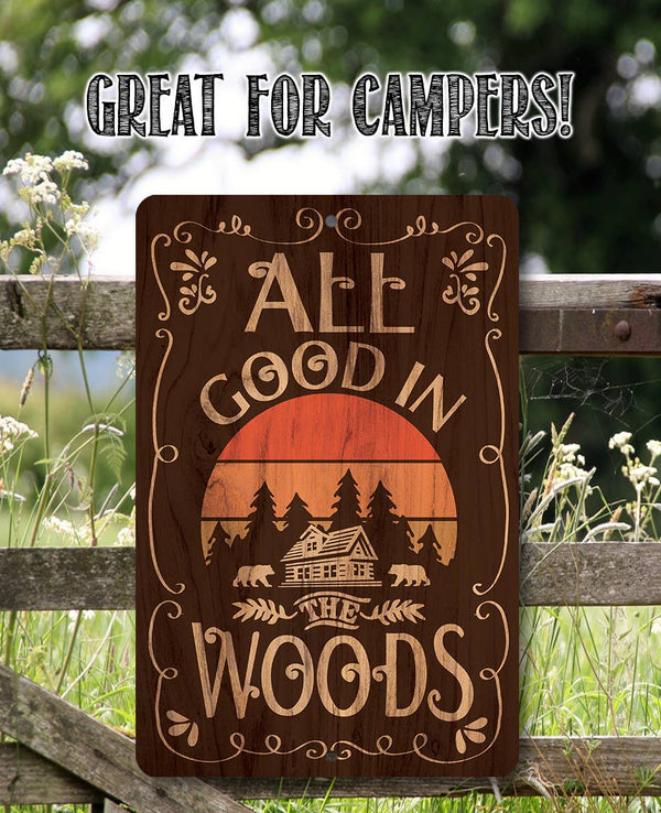 Wooden sign with 'All Good in the Woods' text and sunset design, placed outdoors.