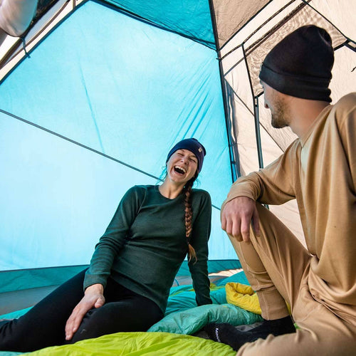 Two people inside a tent, one laughing and the other sitting, with colorful bedding.