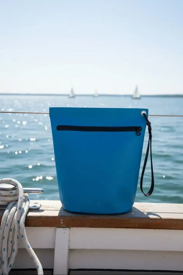 Blue bucket with black zipper on boat deck, ocean and sailboats in background