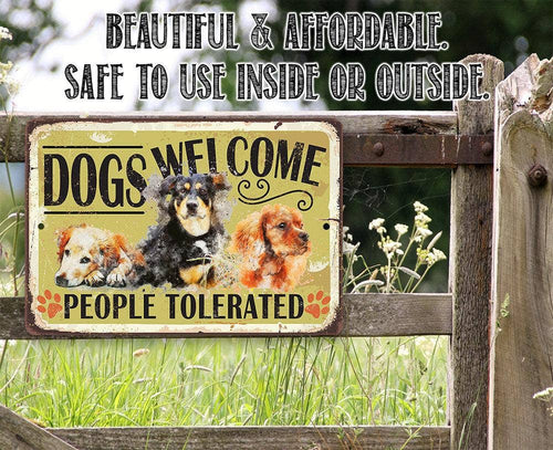 A rectangular metal sign with a distressed cream background reading 'DOGS WELCOME' and 'PEOPLE TOLERATED' with three dog portraits, mounted on a rustic wooden fence outdoors. Above the sign, text reads 'BEAUTIFUL & AFFORDABLE.