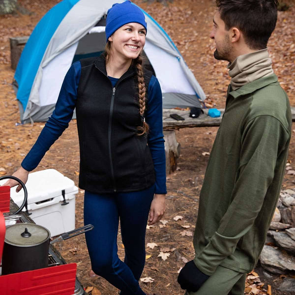 Two people camping outdoors with a tent and cooler in the background.