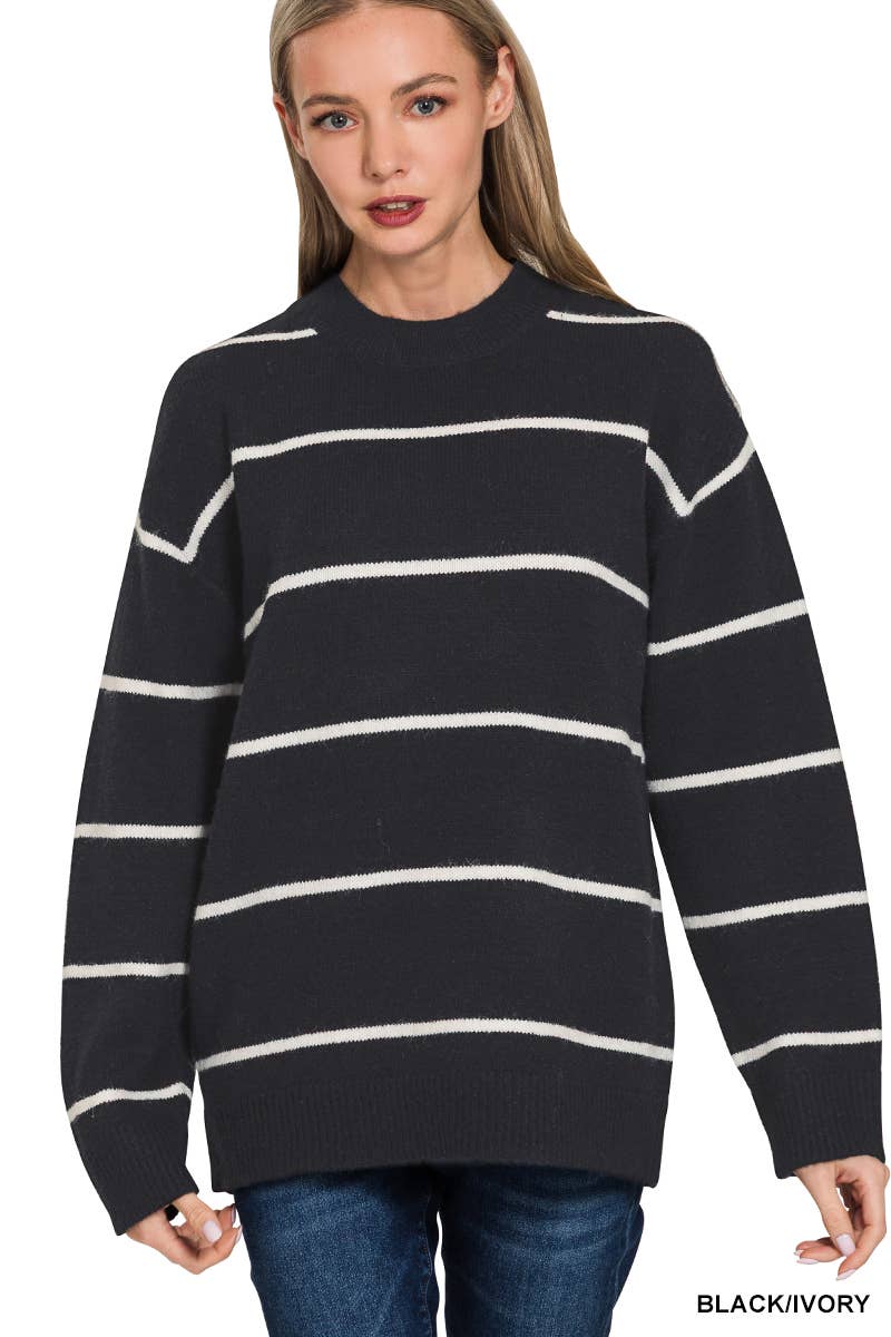 A woman wearing a black knit sweater with horizontal white stripes, paired with blue jeans, against a plain white background.