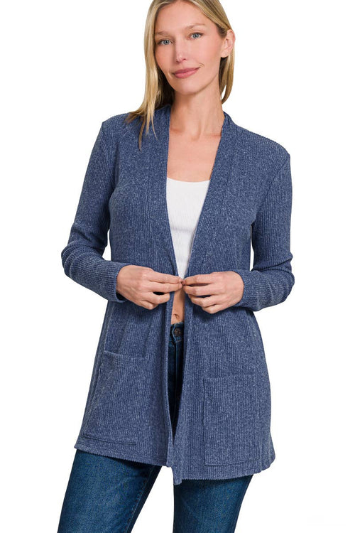 A woman wearing a heathered blue open-front cardigan with front pockets over a white top and blue jeans, photographed against a plain white studio background.