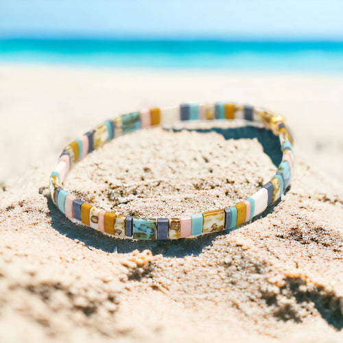 Colorful beaded bracelet on a sandy beach with a clear blue sky.