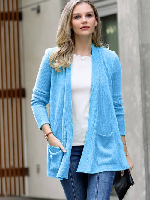 Woman wearing a light blue cardigan over a white shirt and jeans, standing outdoors.