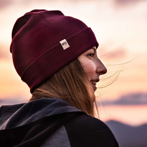 Person wearing a maroon beanie with a logo against a sunset sky
