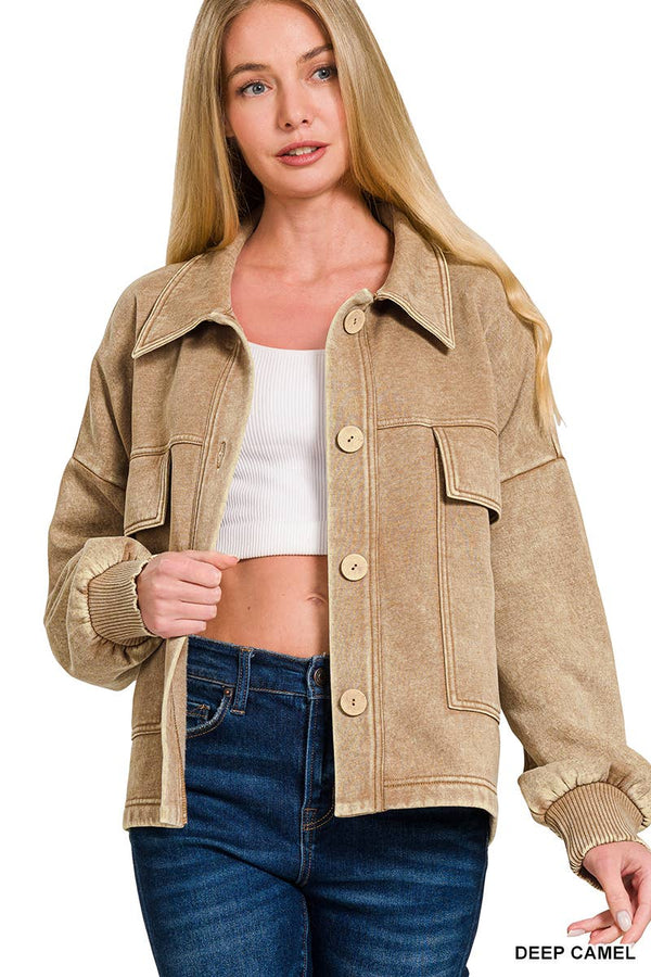 A woman wearing a cropped tan suede-like jacket with large buttons and flap pockets, styled over a white crop top and blue jeans on a white background.