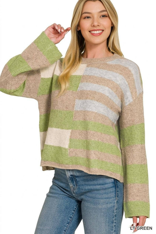 A woman wearing a fuzzy knit sweater with wide horizontal stripes in light green, beige, cream, and light gray, paired with blue jeans, against a plain white background.