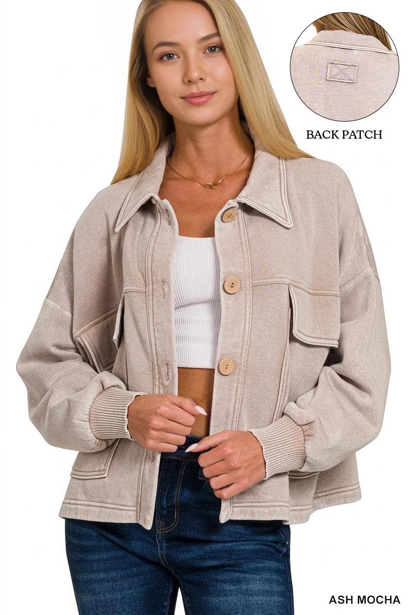 A woman wearing an oversized light ash-mocha corduroy jacket with button-front closure and flap chest pockets, paired with a white ribbed crop top and dark blue jeans. A circular inset at the top right shows the back patch of the jacket.