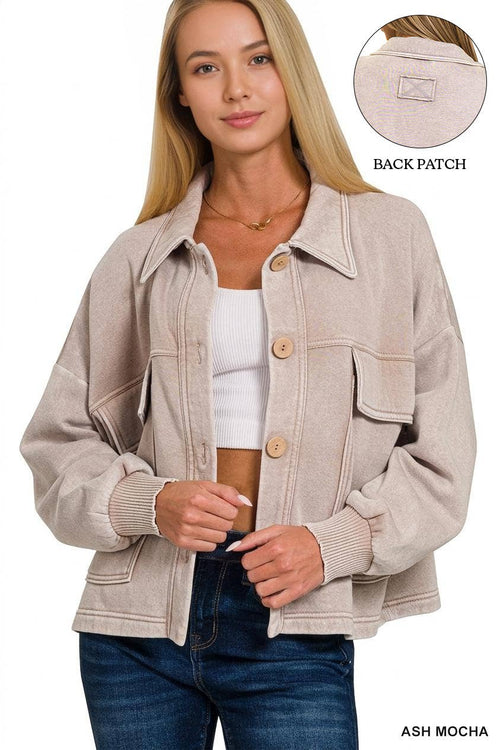 A woman wearing an oversized light ash-mocha corduroy jacket with button-front closure and flap chest pockets, paired with a white ribbed crop top and dark blue jeans. A circular inset at the top right shows the back patch of the jacket.