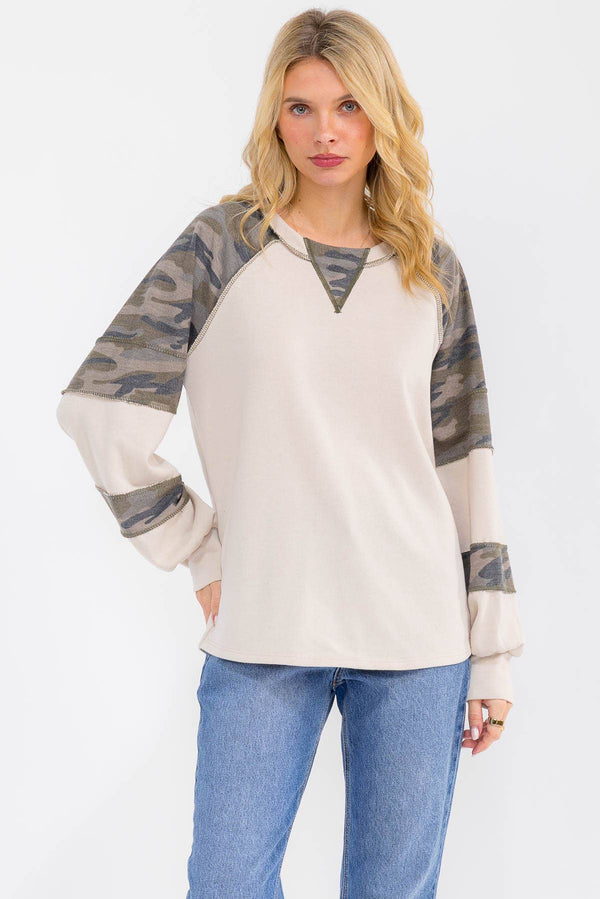 Woman wearing a cream and camouflage long-sleeve top with blue jeans on a white background